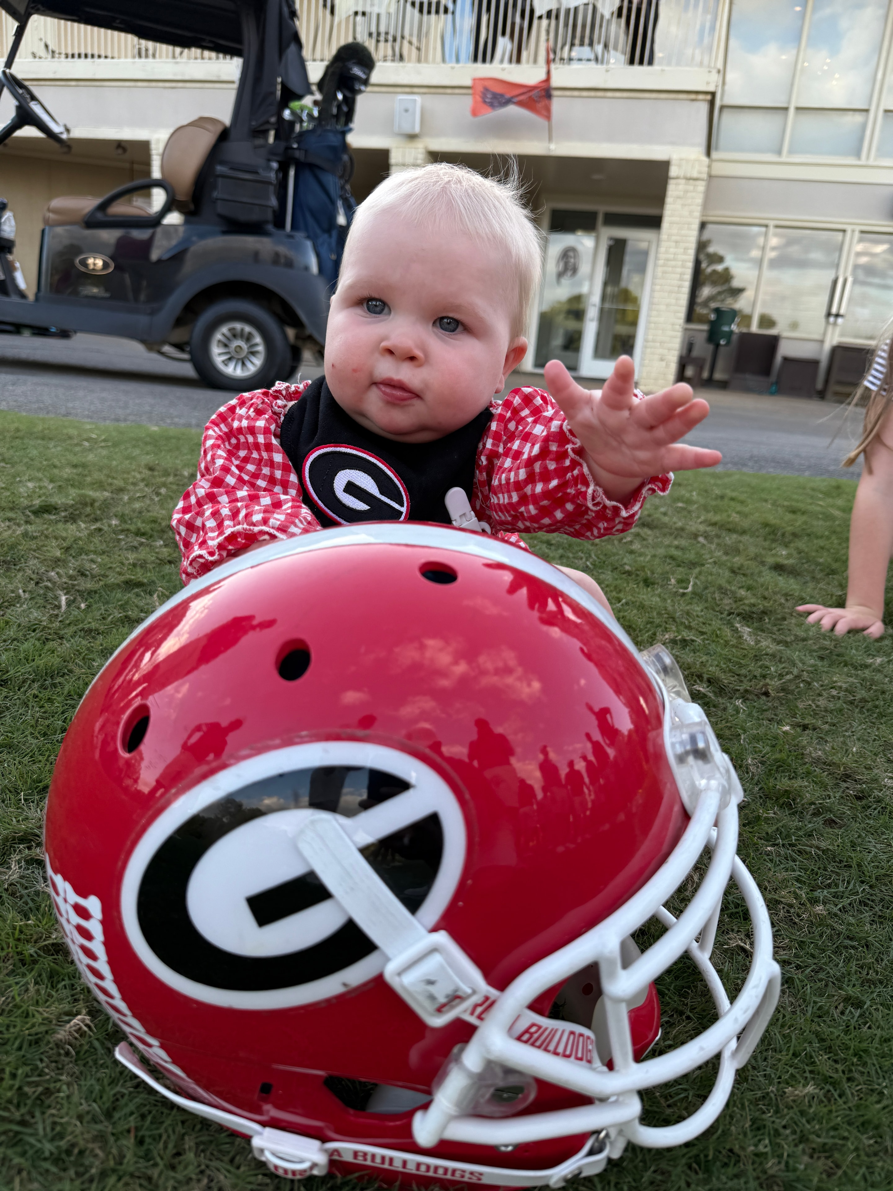 Baby in a Georgia onesie next to a red football helmet at the tournament