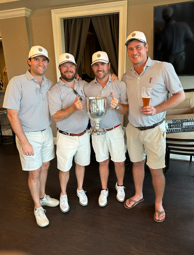 Four players in matching polos holding the Dooley-Dye Cup indoors