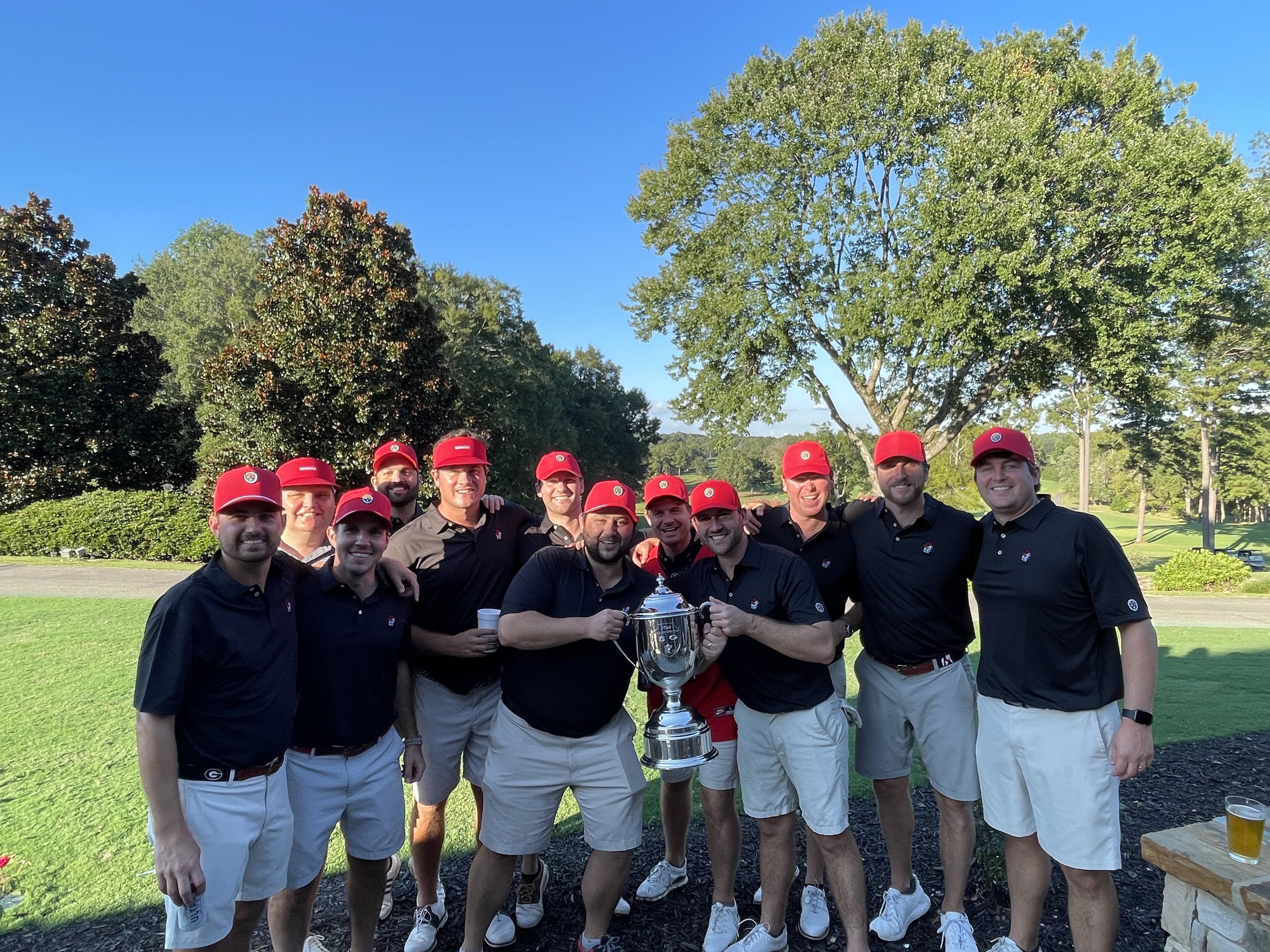 Team Dooley in red caps holding the Cup on the clubhouse grounds, 2025