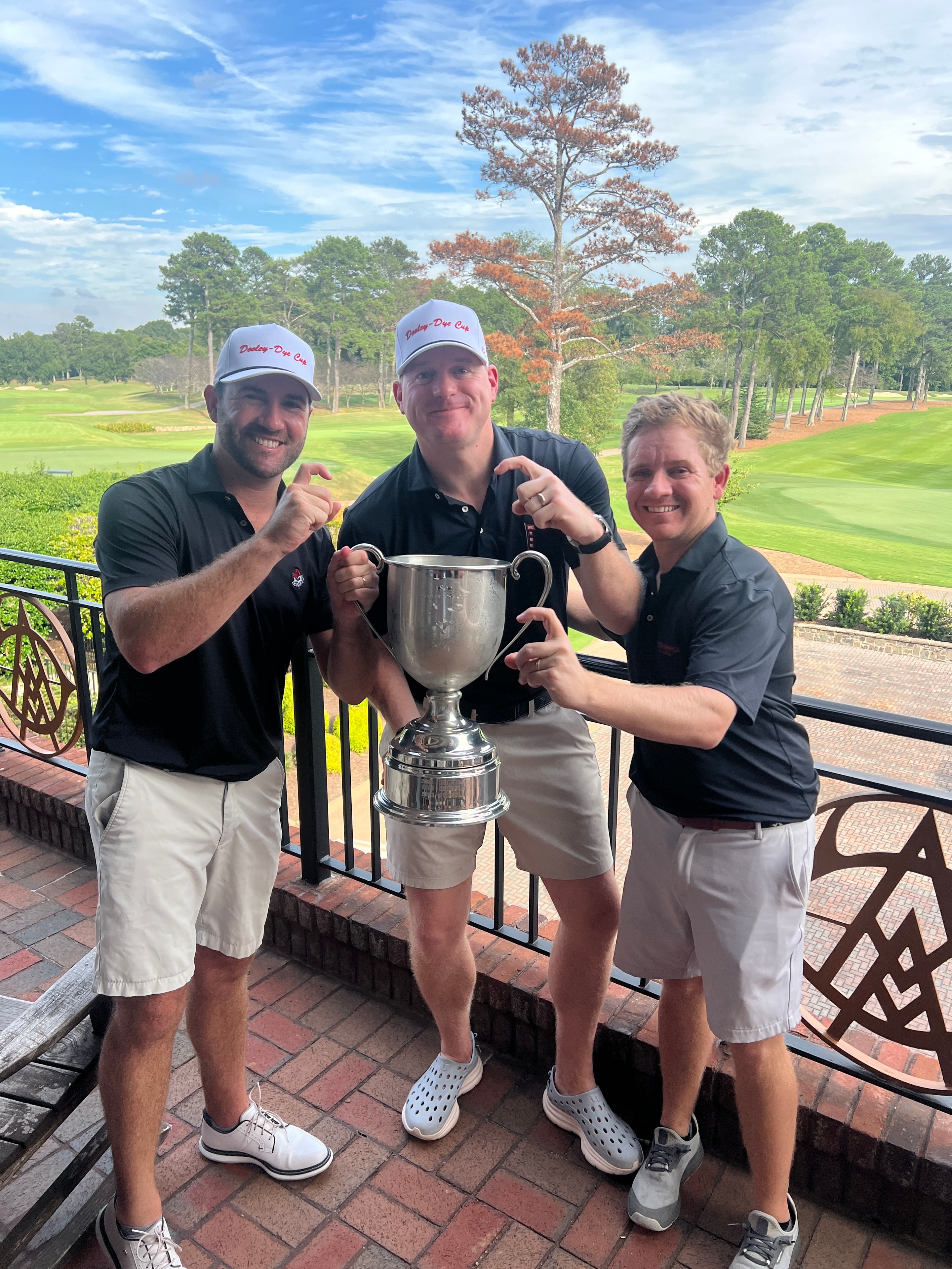 Three players celebrating with the Dooley-Dye Cup on the patio