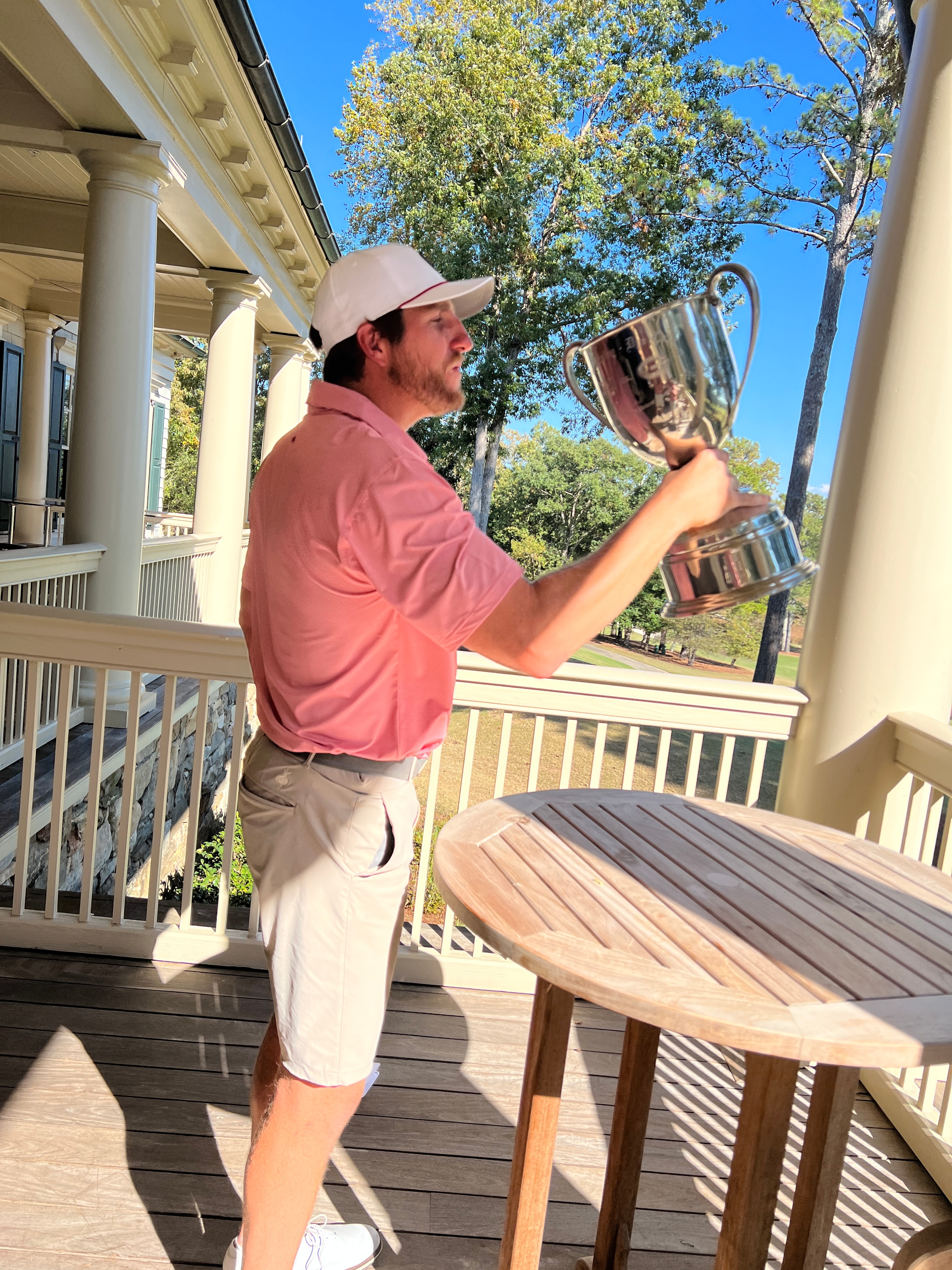 Player lifting the Dooley-Dye Cup overhead on the clubhouse patio