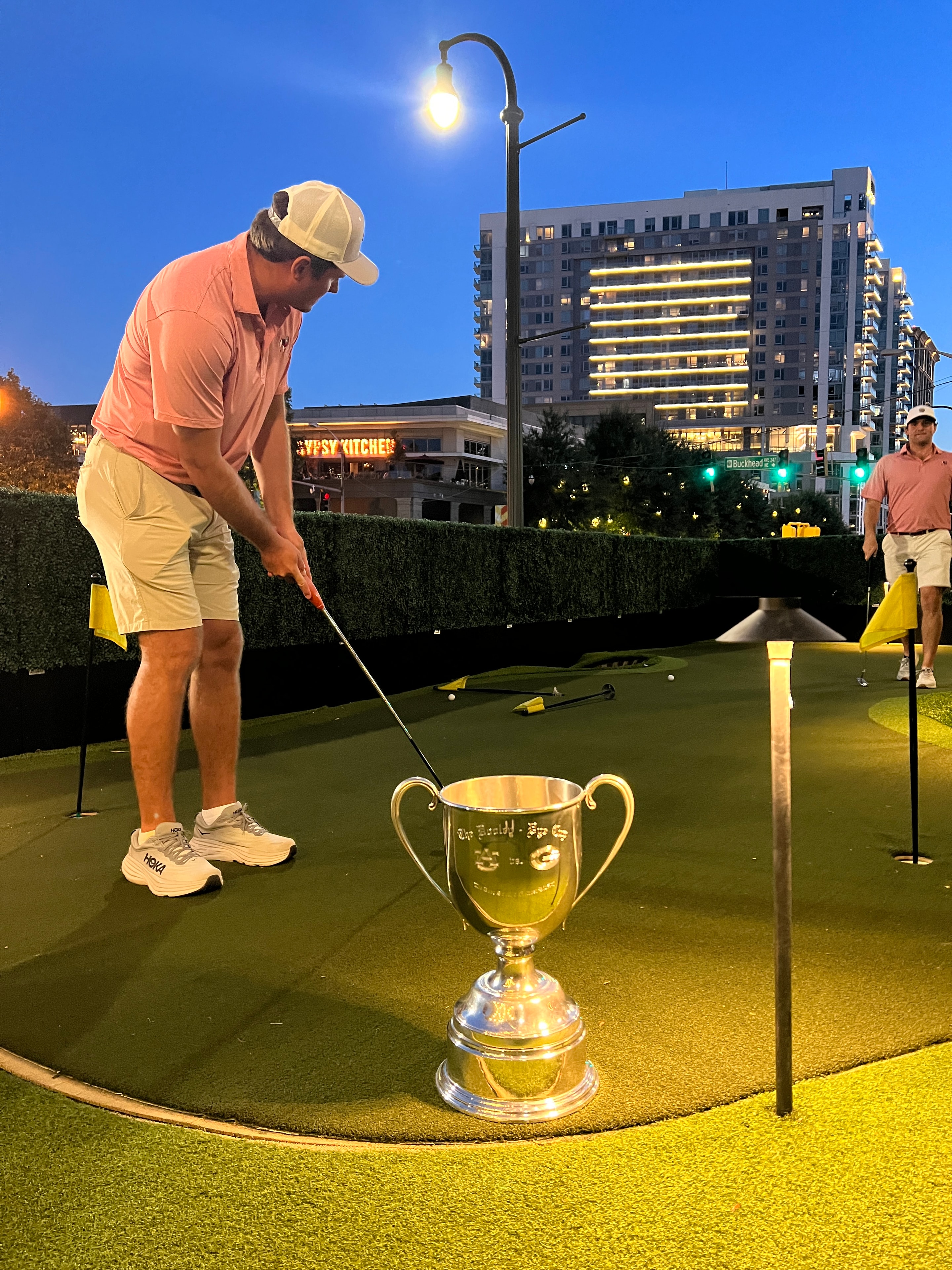 Player putting next to the Dooley-Dye Cup under city lights at night