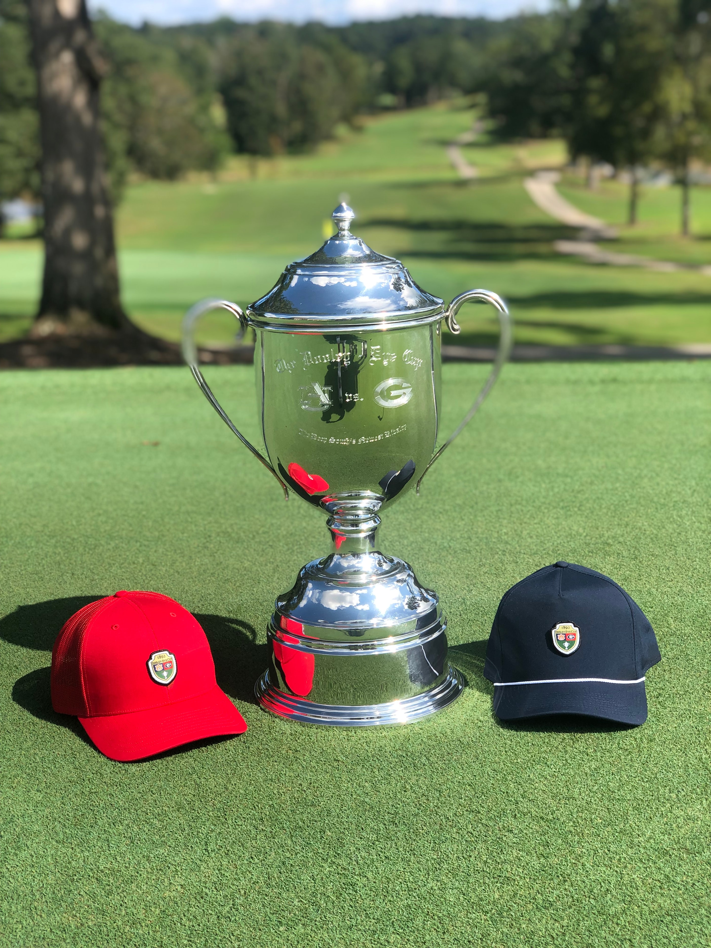 Dooley-Dye Cup trophy flanked by red and navy caps on the green