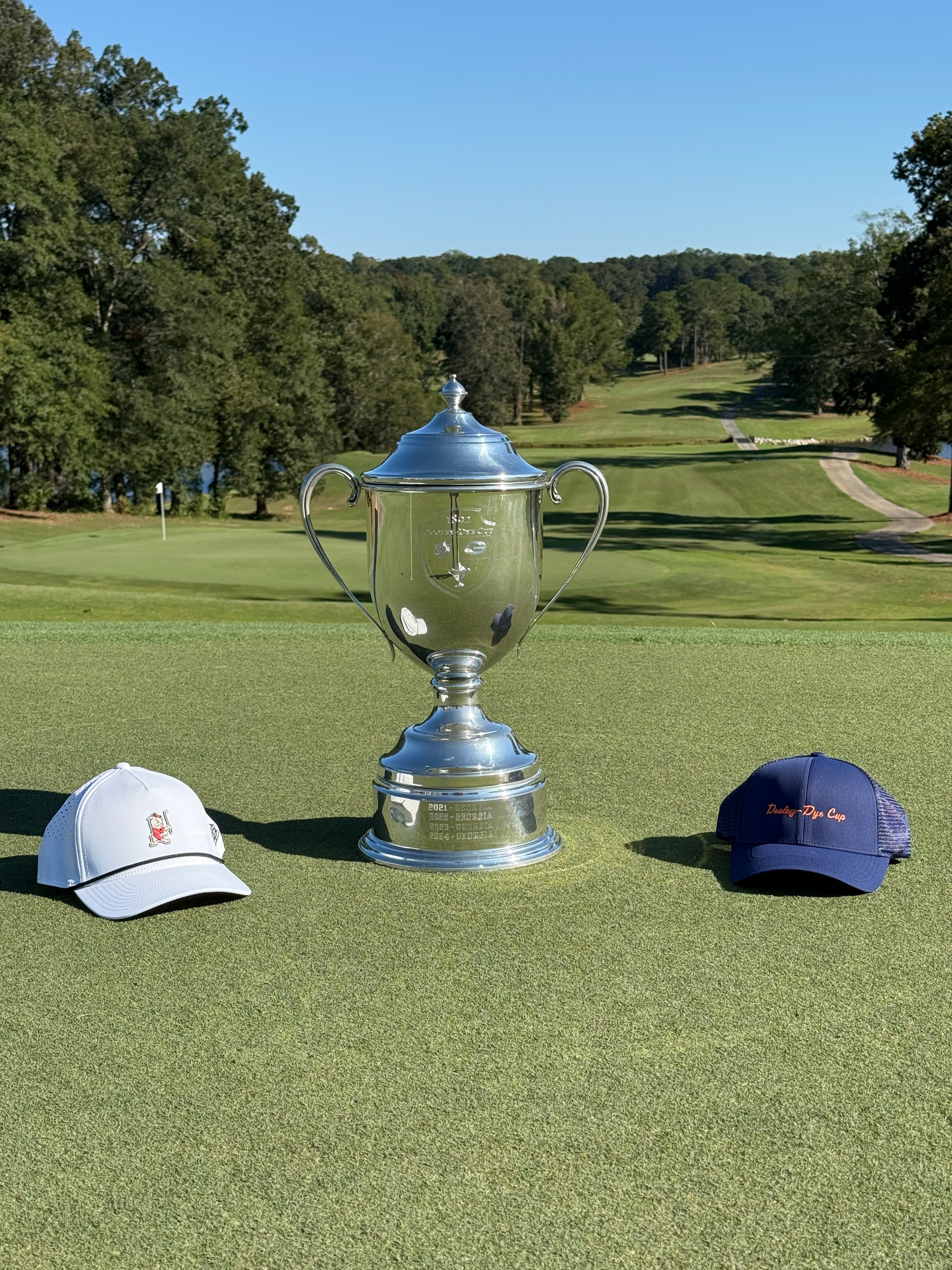 Dooley-Dye Cup trophy on the green flanked by a navy and white cap
